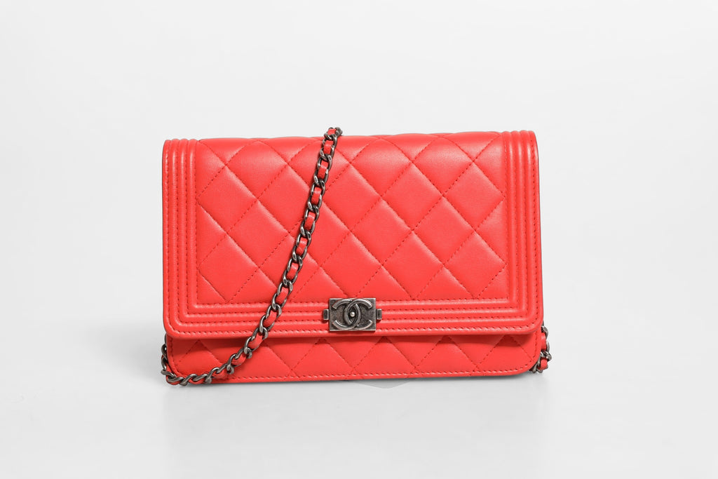 Portefeuille Chanel Boy en cuir d'agneau rouge avec chaîne, élégant et sophistiqué, visible en détail dans cette image.