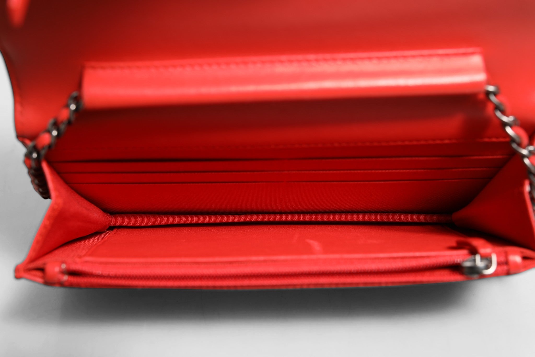Portefeuille Chanel Boy en cuir d'agneau rouge avec chaîne, élégant et sophistiqué, visible avec détails du cuir et de la chaîne.