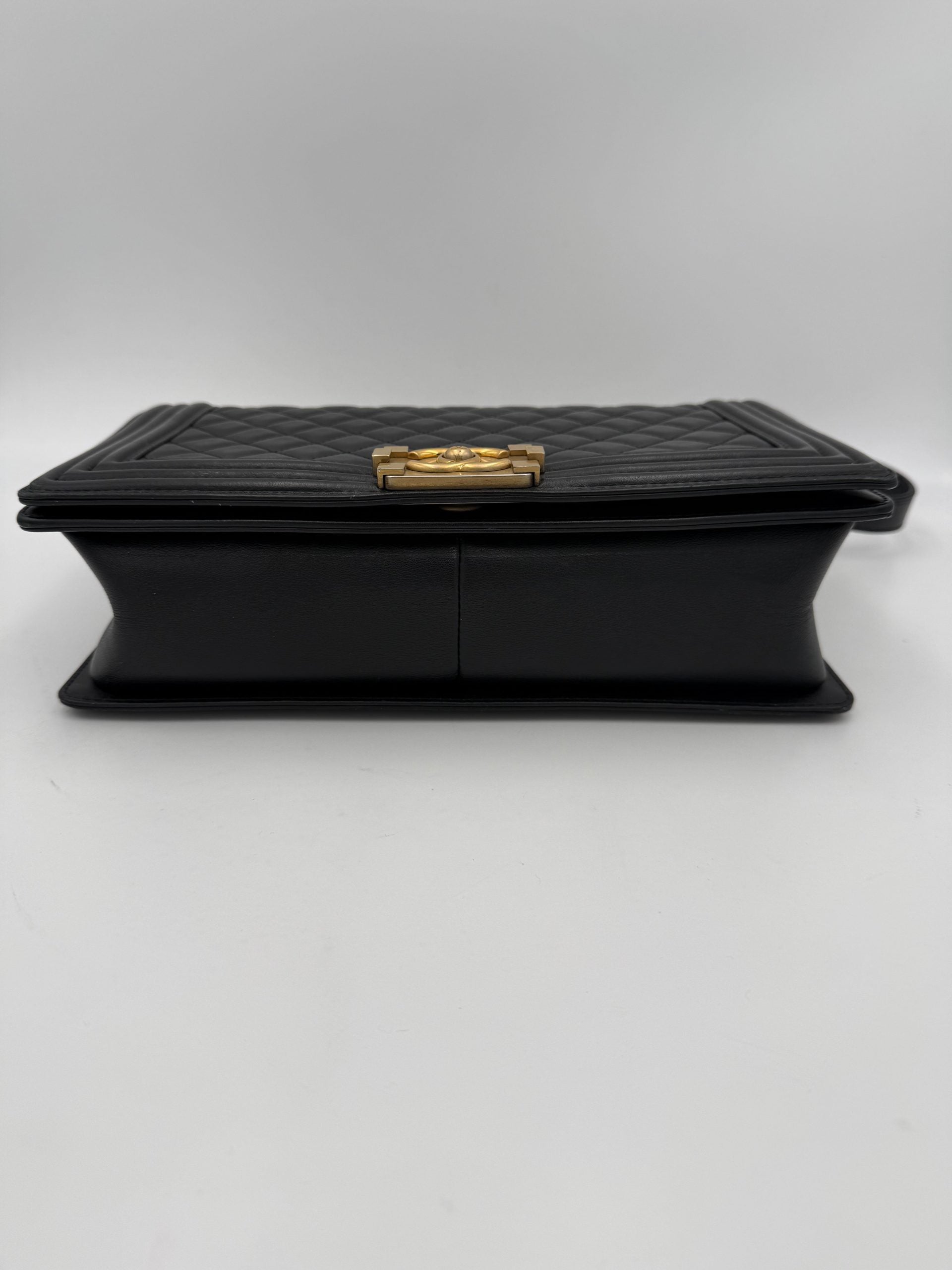 Grand sac à main Chanel Boy de grande taille, en cuir noir avec chaîne en métal et logo Chanel visible.