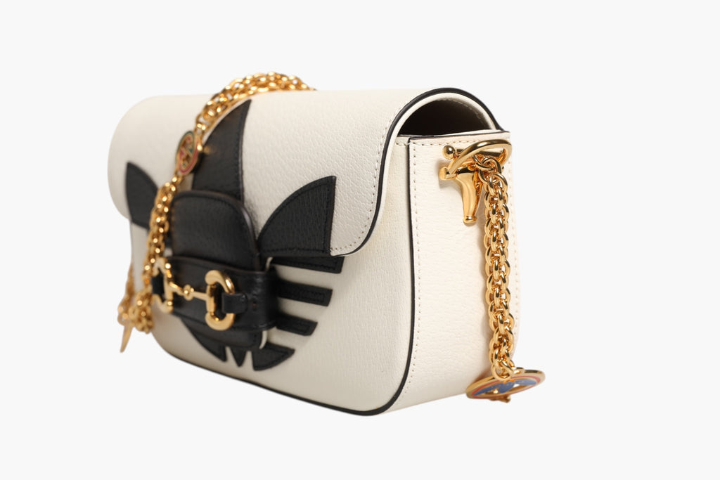 Sac à bandoulière Gucci x Adidas Horsebit 1955 en cuir blanc et noir, style élégant avec détails en métal.