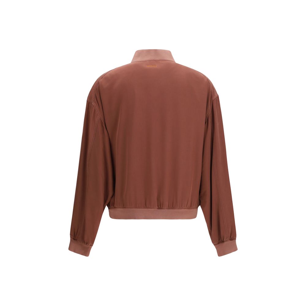 Veste bomber en soie bordeaux de Versace avec logo emblématique, coupe élégante et détails luxueux.