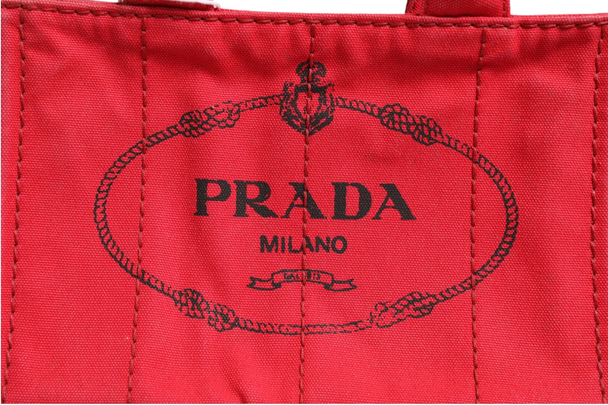 Sac Prada Canapa Mini en toile canvas, compact et élégant, avec poignées en cuir et logo Prada visible sur le devant.