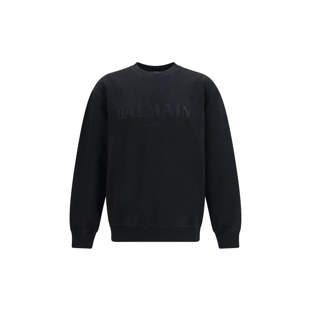 Sweatshirt en coton noir Balmain, décontractée, avec logo visible, porté sur un modèle dans un environnement lumineux.