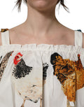 Top blanc Dolce & Gabbana à imprimé coq en popeline, décolleté épaules, style élégant et tendance.
