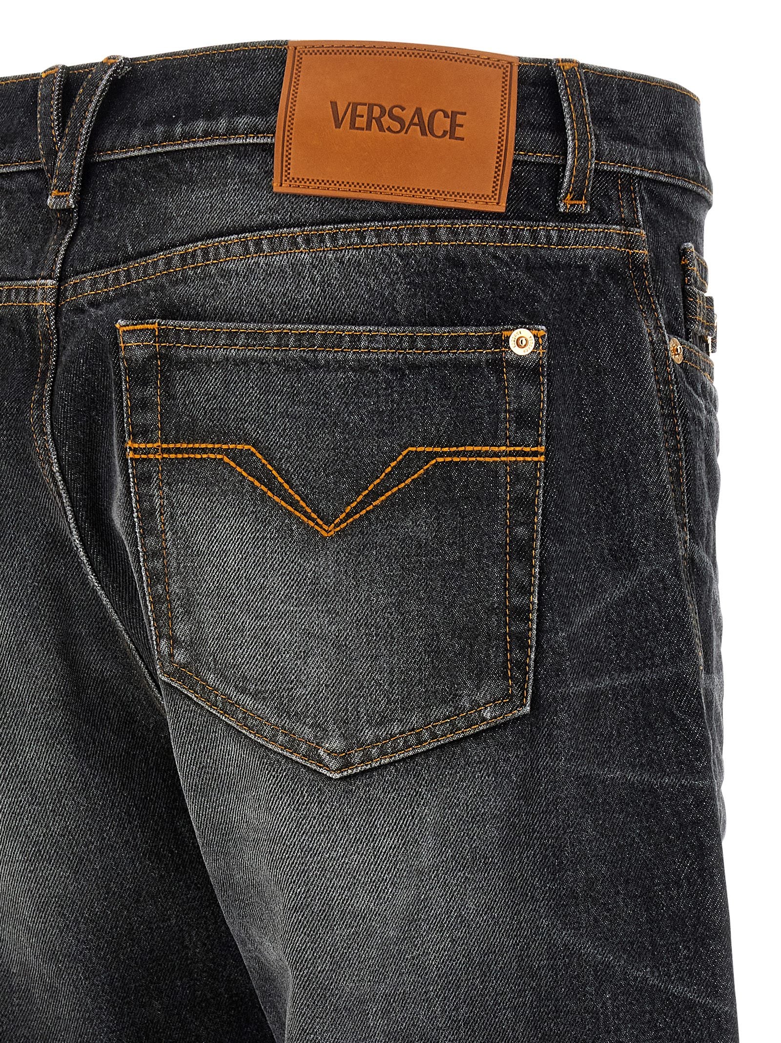 Jeans droits en coton noir de la marque Versace, vue de face, avec détails de couture visibles.