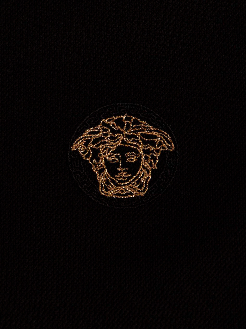 Chemise polo en coton noir de la marque Versace, visible avec col classique et logo distinctif sur la poitrine.