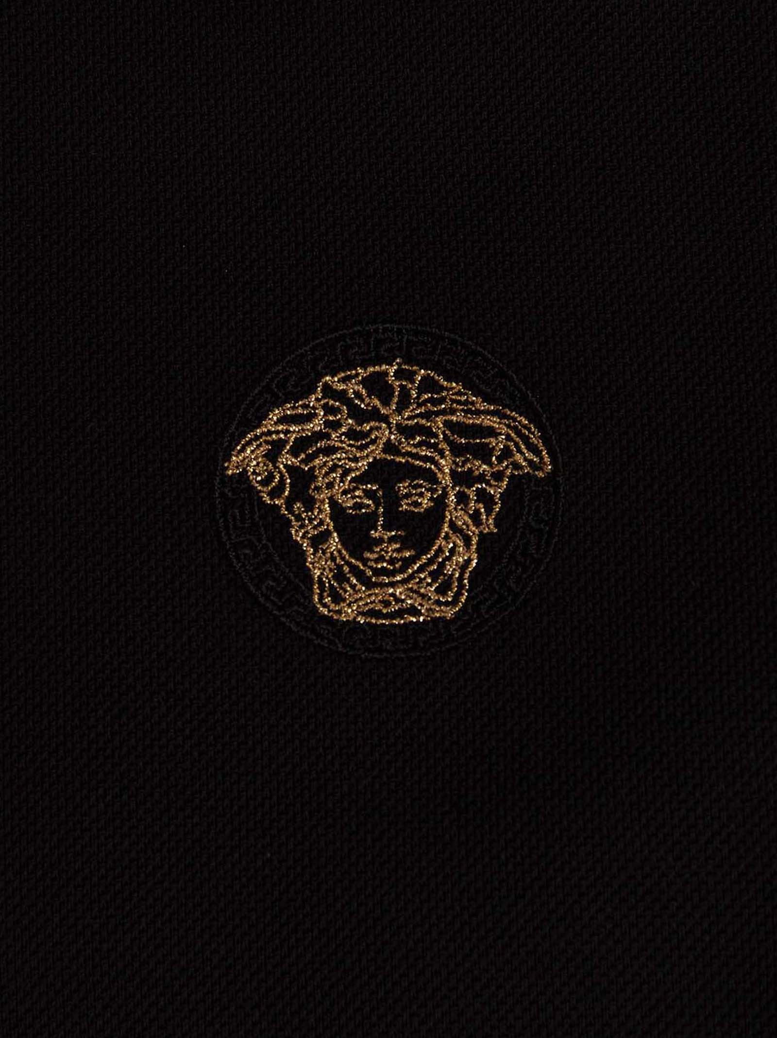 Chemise polo en coton noir de la marque Versace, visible avec col classique et logo distinctif sur la poitrine.