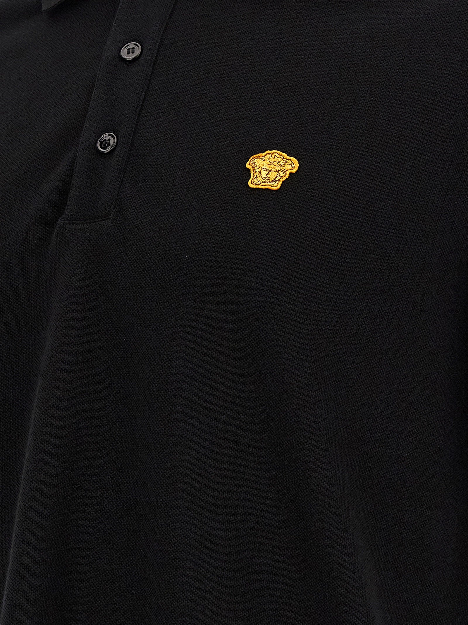 Chemise polo noire en coton Versace avec logo distinctif, manches courtes et col classique, vue de face.