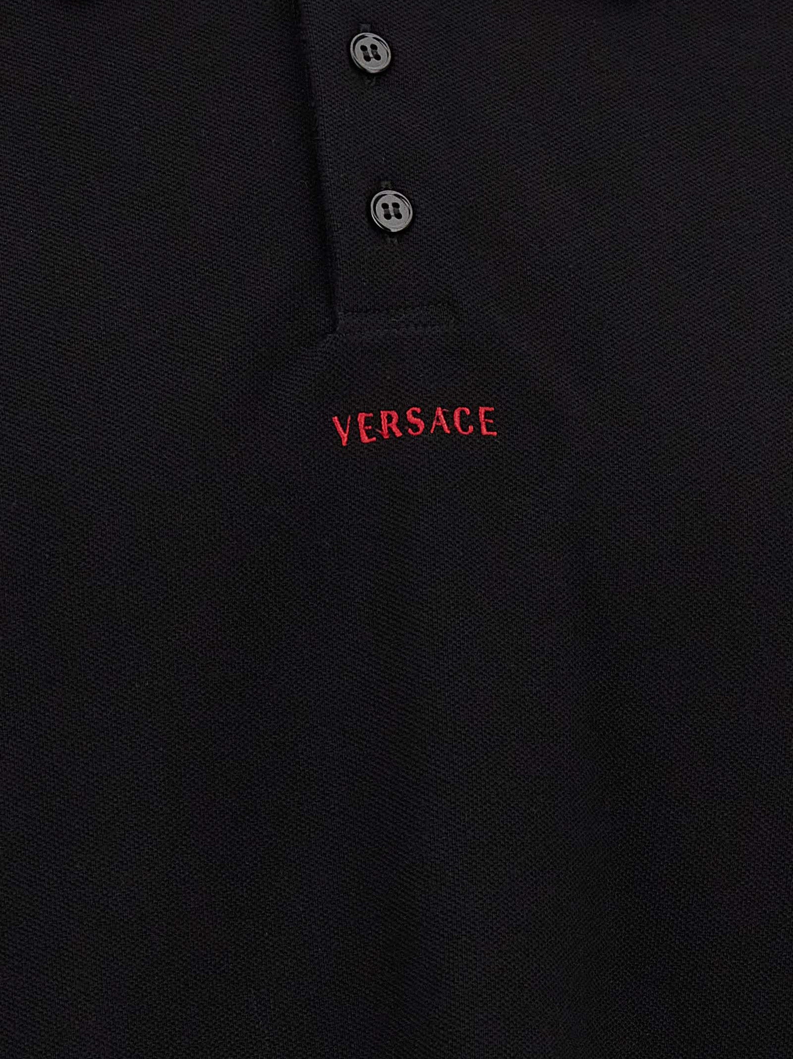 Chemise polo noire en coton de la marque Versace, avec logo distinctif et design élégant, sur un fond neutre.