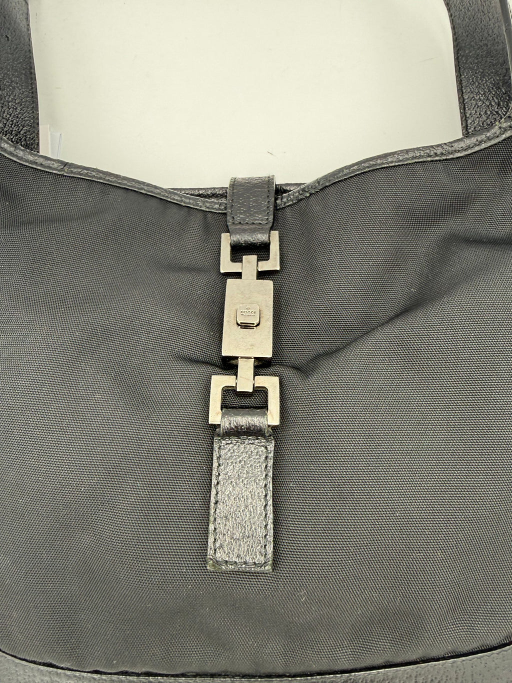 Sac à main Gucci Jackie en cuir et toile, avec bandoulière et logo emblématique, visible sur fond neutre.