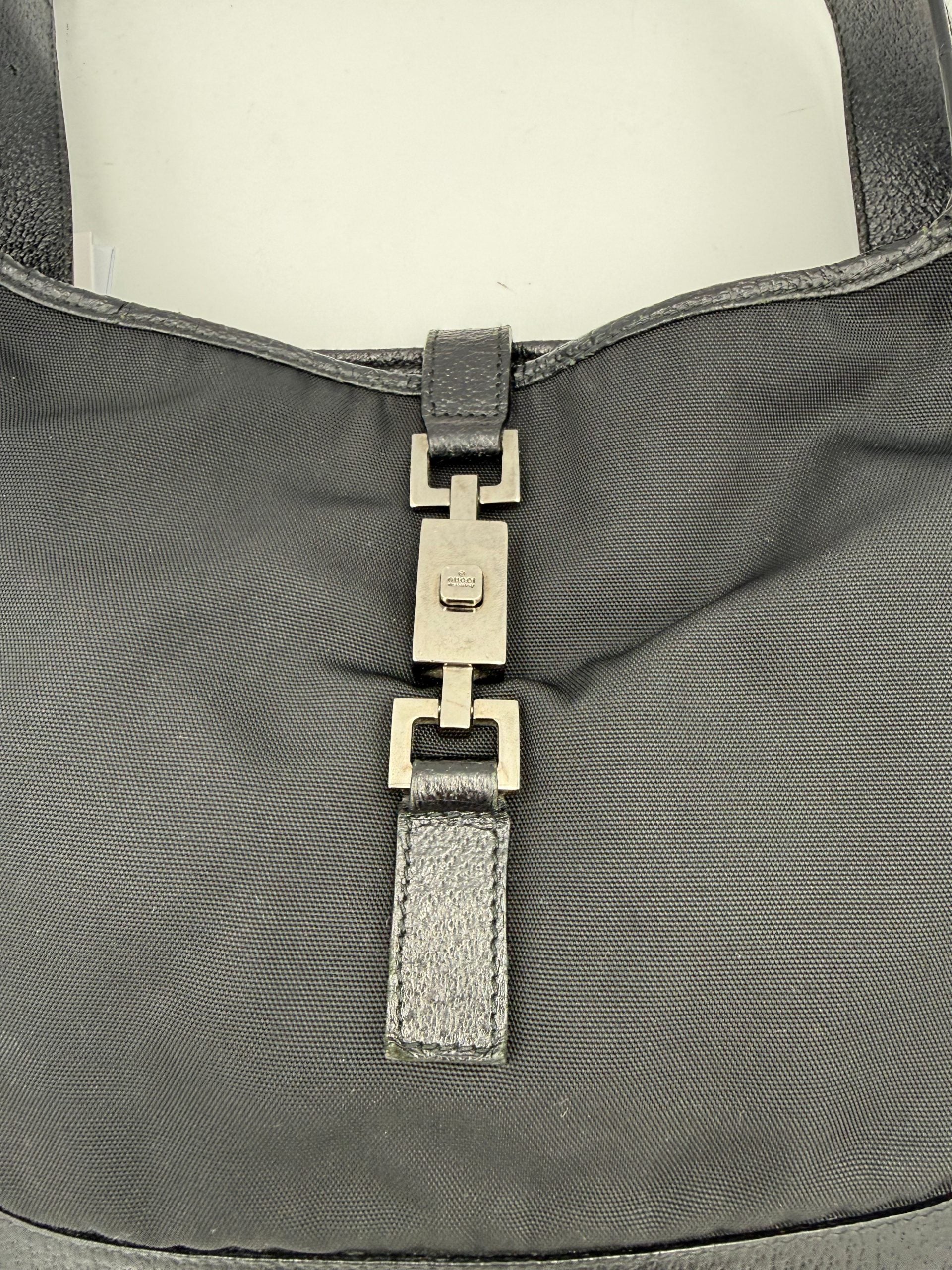 Sac à main Gucci Jackie en cuir et toile, avec bandoulière et logo emblématique, visible sur fond neutre.