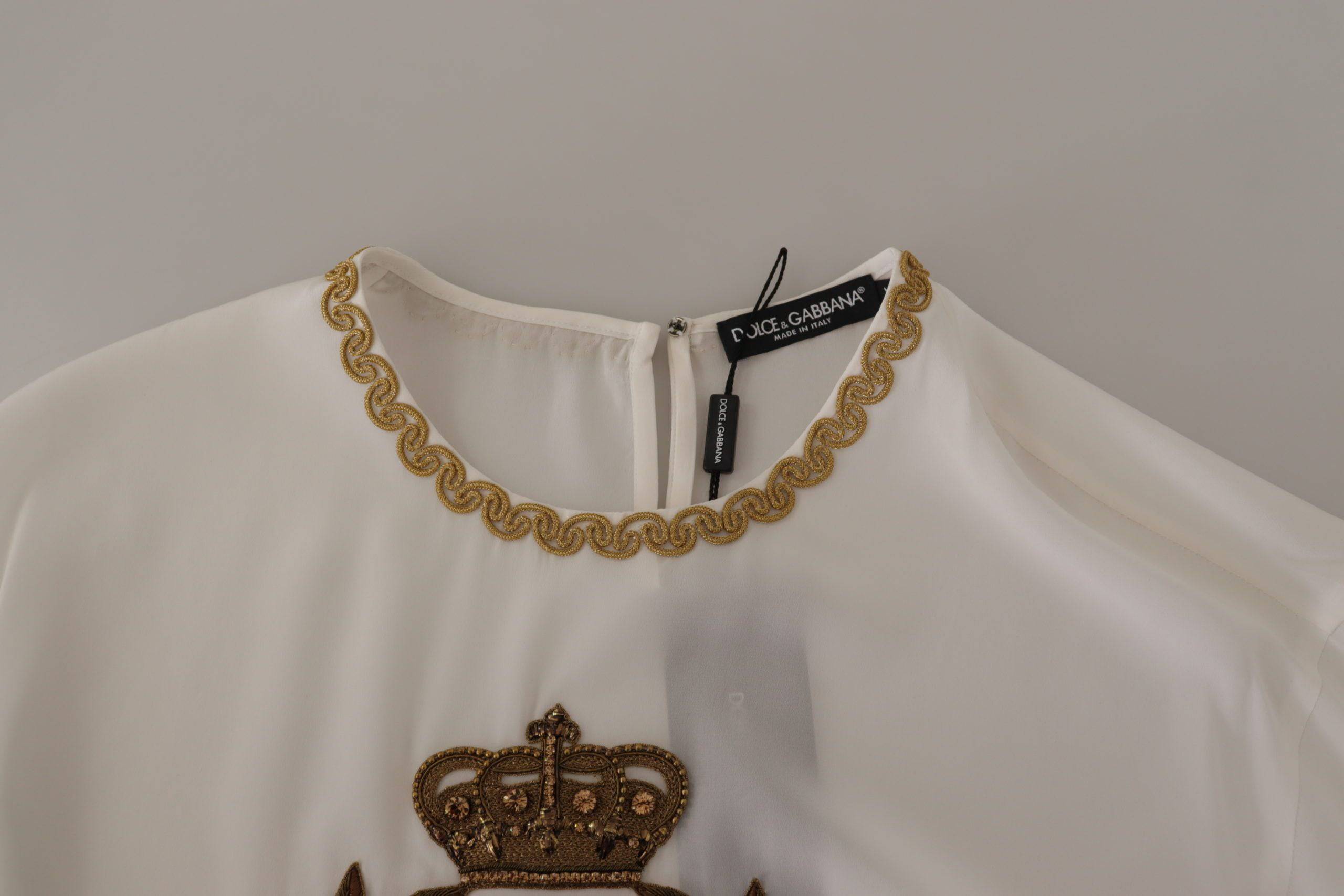 Chemisier blanc en soie Dolce & Gabbana avec broderie en or, détails de couronne en cristal, style élégant et sophistiqué.