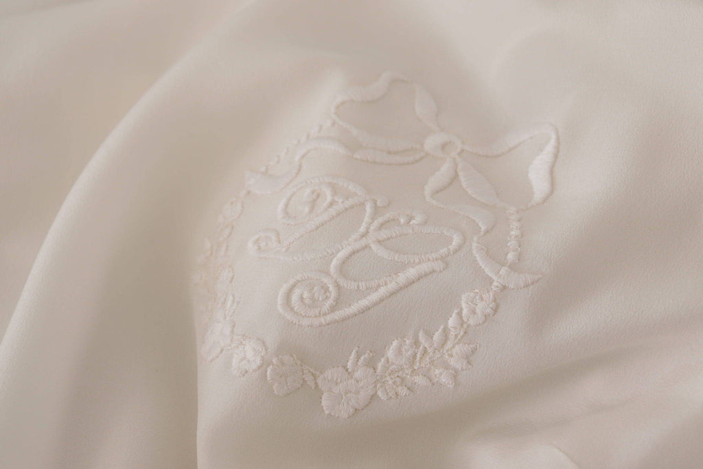 Chemise longue en soie blanche Dolce & Gabbana avec logo DG brodé et manches longues, élégante et sophistiquée.