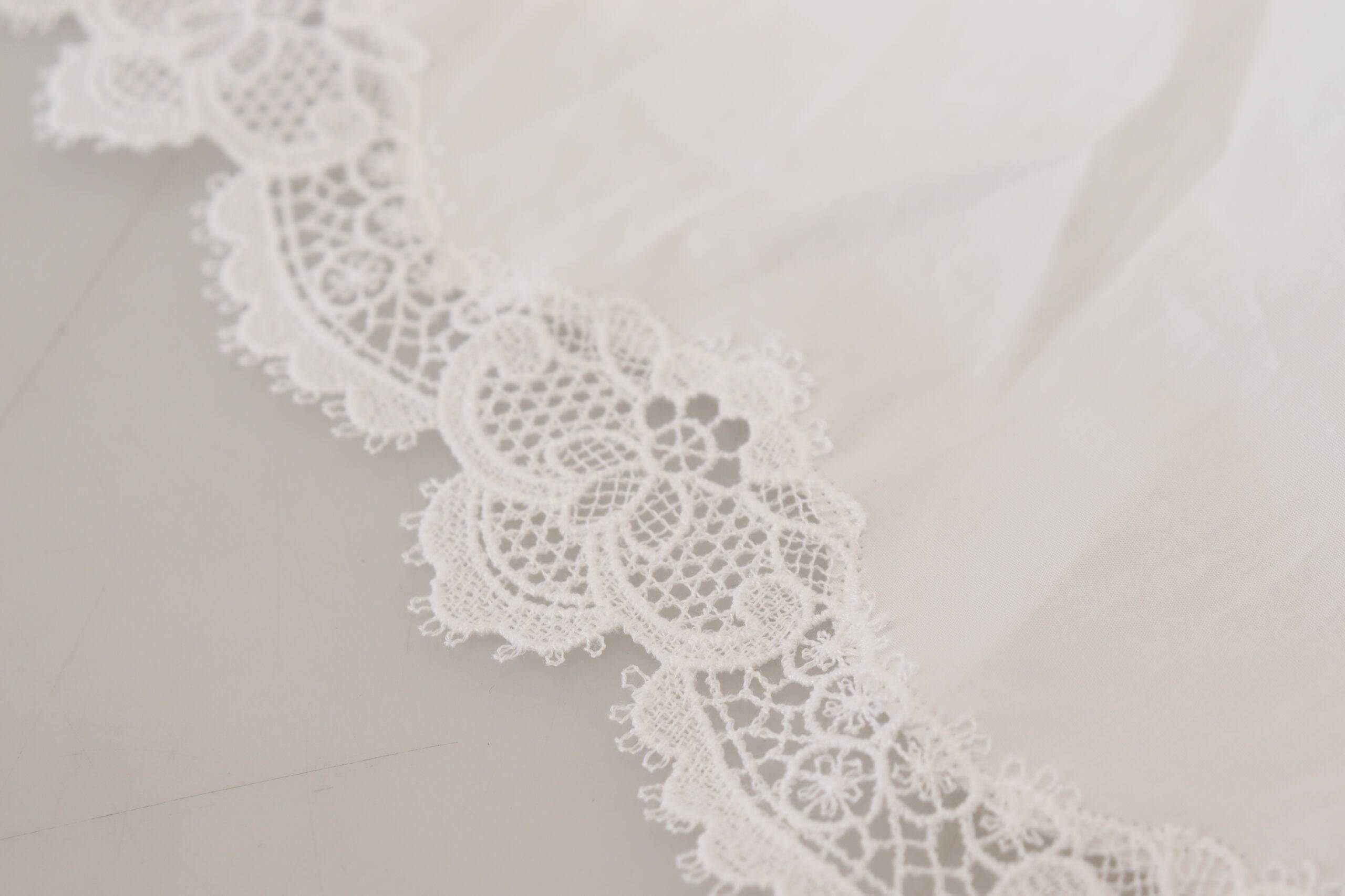 Blouse blanche en coton avec dentelle, col roulé Dolce & Gabbana, détail élégant et tissu léger visible sur l'image.