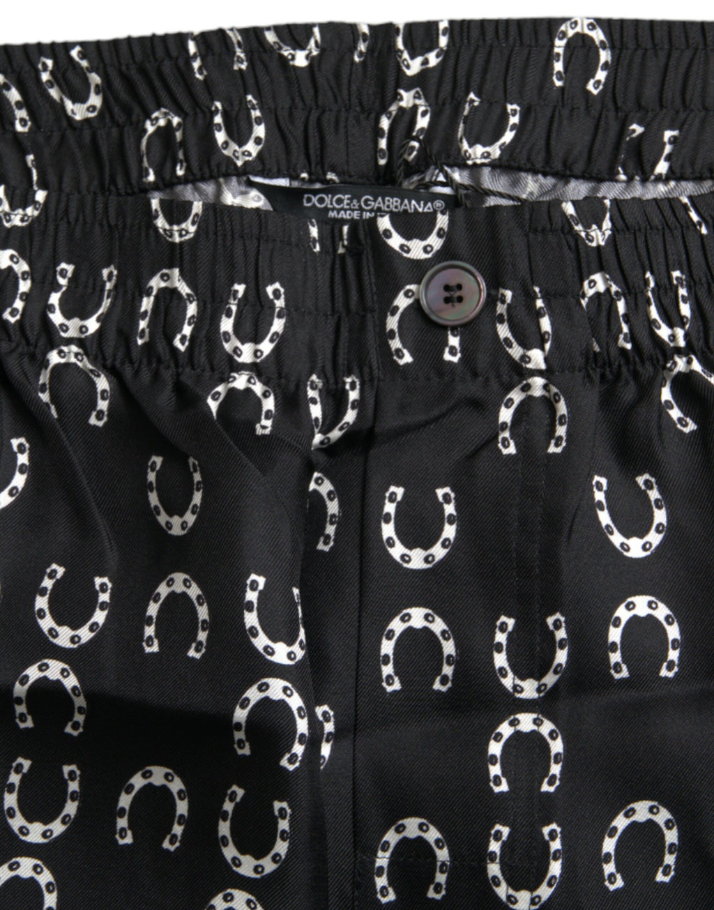 Pantalons en soie Dolce & Gabbana avec motif fer à cheval noir, élégants et sophistiqués, visibles en détail dans l'image.