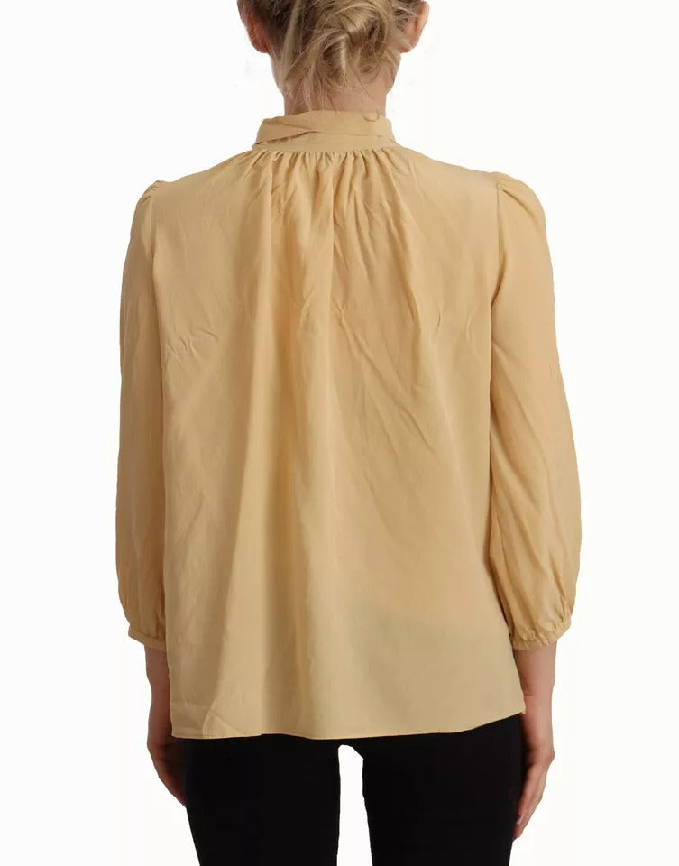 Chemise en soie Dolce & Gabbana avec col ascot moutarde, haut élégant et sophistiqué, visible en gros plan.