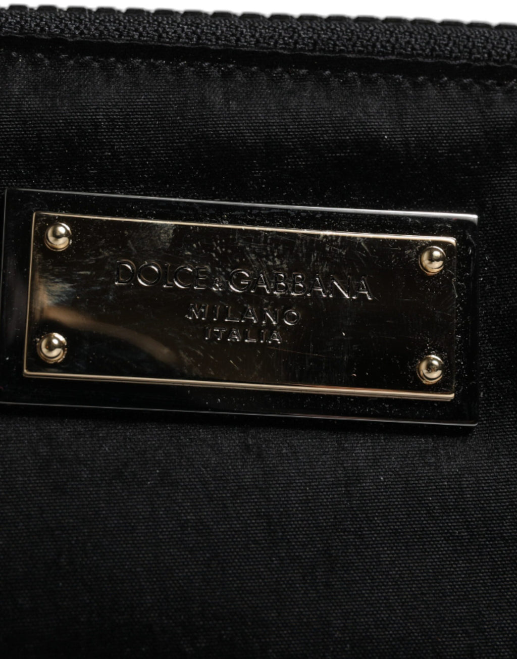Porte-clés en nylon noir Dolce & Gabbana avec plaque logo, attaché à une pochette ou clutch élégante, vue rapprochée.