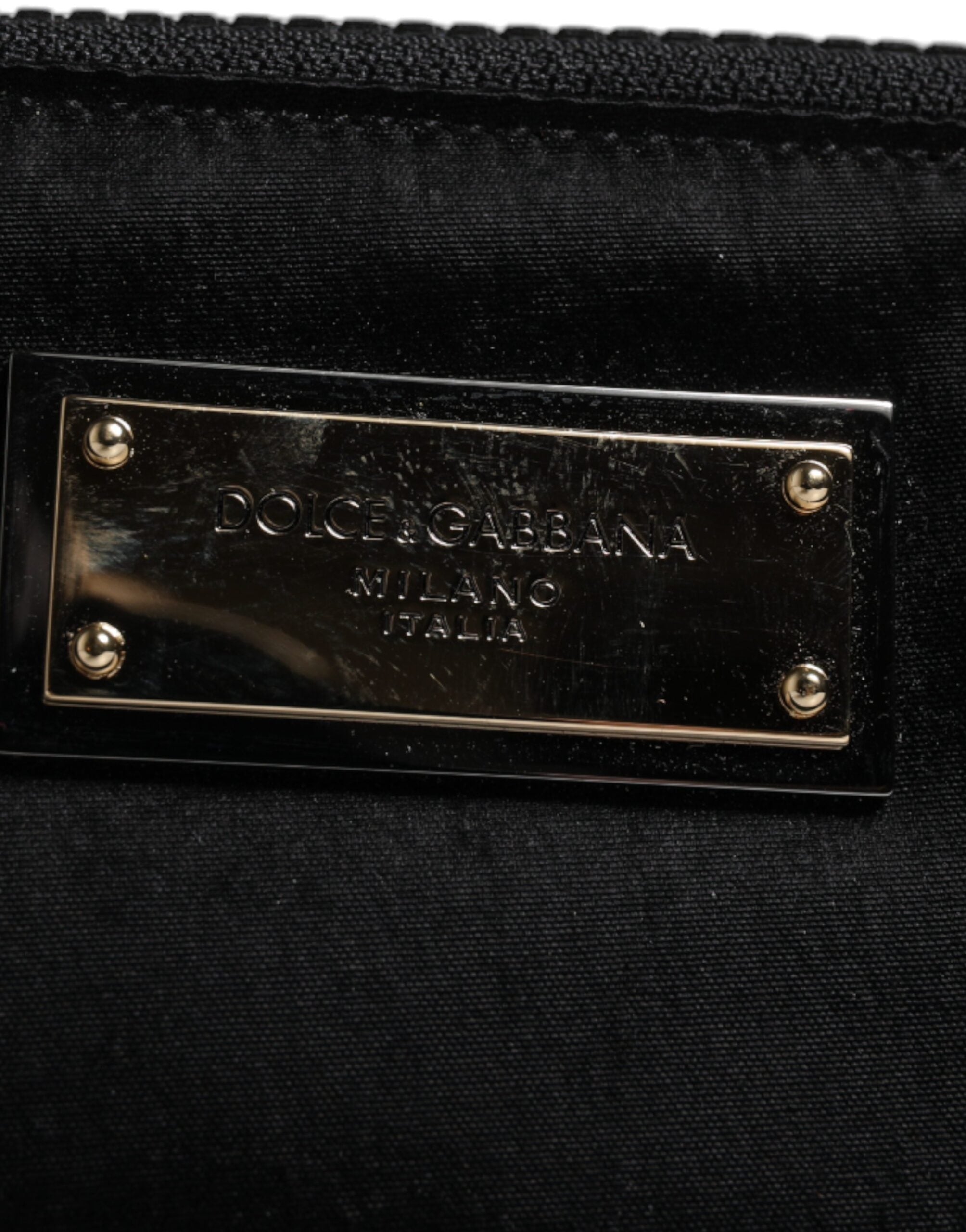 Porte-clés en nylon noir Dolce & Gabbana avec plaque logo, attaché à une pochette ou clutch élégante, vue rapprochée.