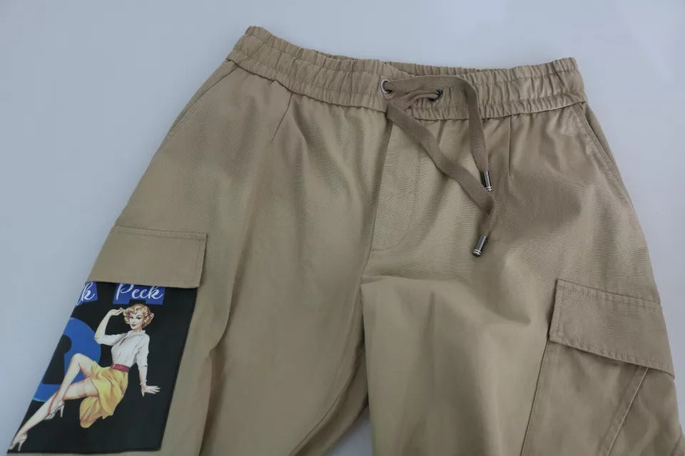 Pantalons cargo beiges Dolce & Gabbana avec imprimé pin-up, style décontracté et détails modernes visibles sur l'image.