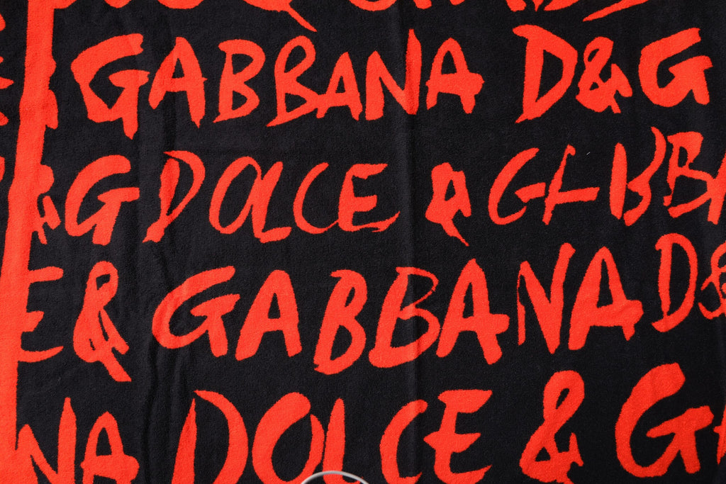 Serviette de plage en coton noir et rouge avec logo Dolce & Gabbana, affichant un motif imprimé élégant et moderne.