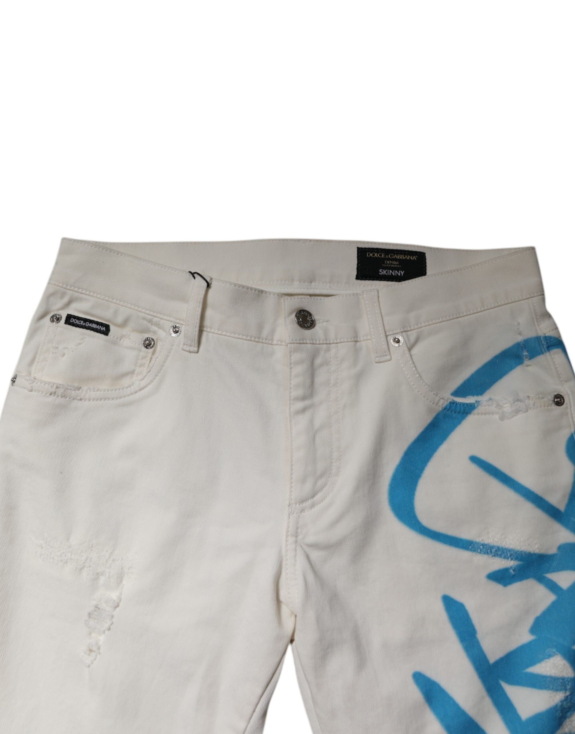 Jeans skinny déchirés et graffiti blanc de Dolce & Gabbana, en denim tendance, visibles avec détails déchirés et motifs artistiques.