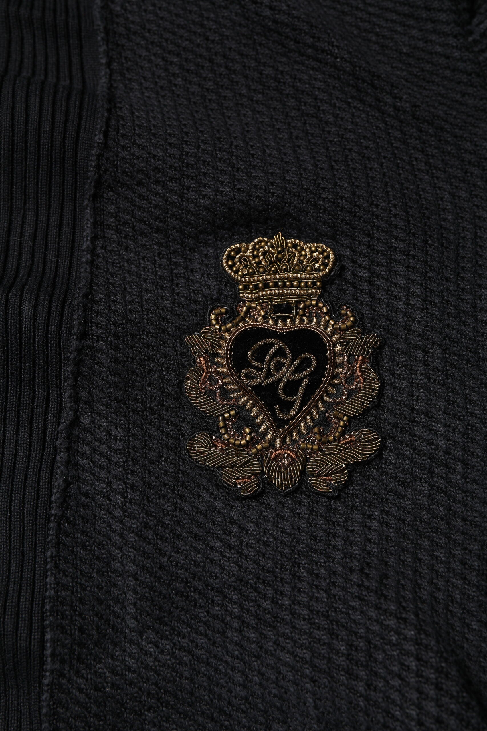 Pull en soie noir Dolce & Gabbana avec boutons, motif héraldique élégant et détails raffinés visible sur l'image.