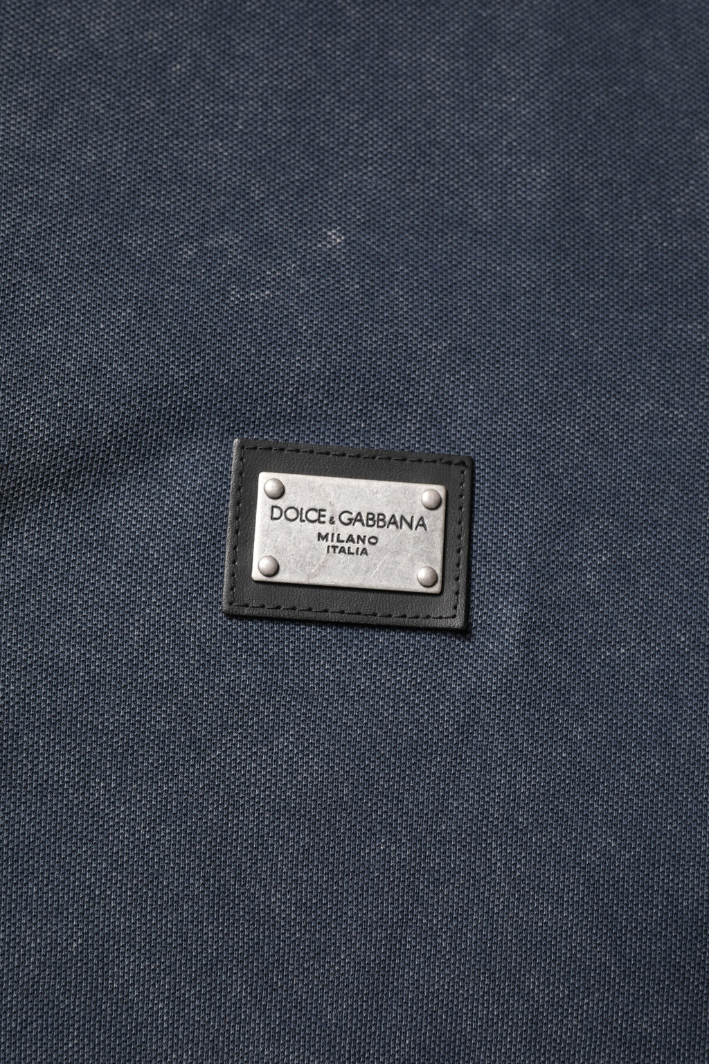 Polo homme Dolce & Gabbana en coton bleu foncé avec logo et plaque décorative, style élégant et décontracté.