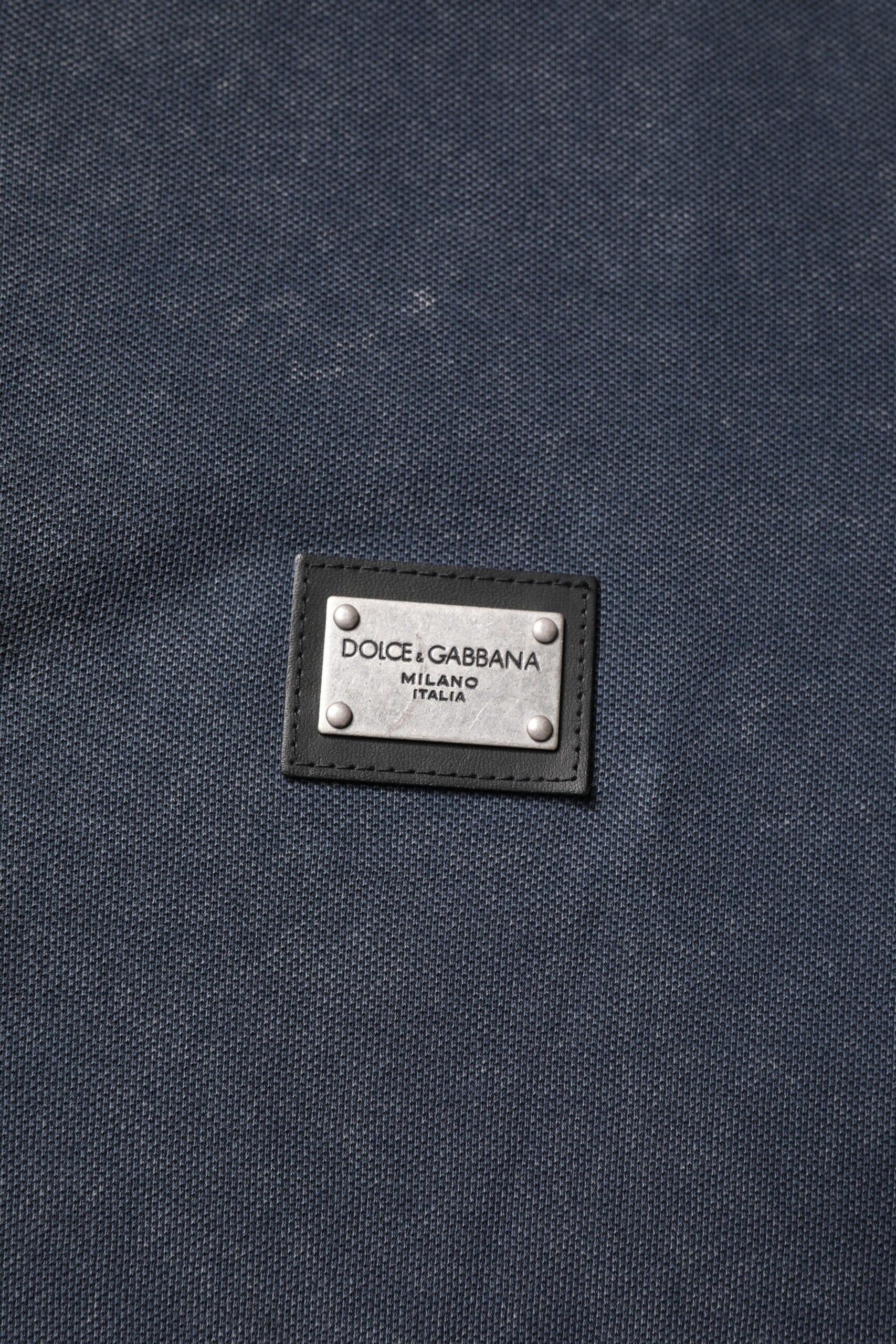 Polo homme Dolce & Gabbana en coton bleu foncé avec logo et plaque décorative, style élégant et décontracté.