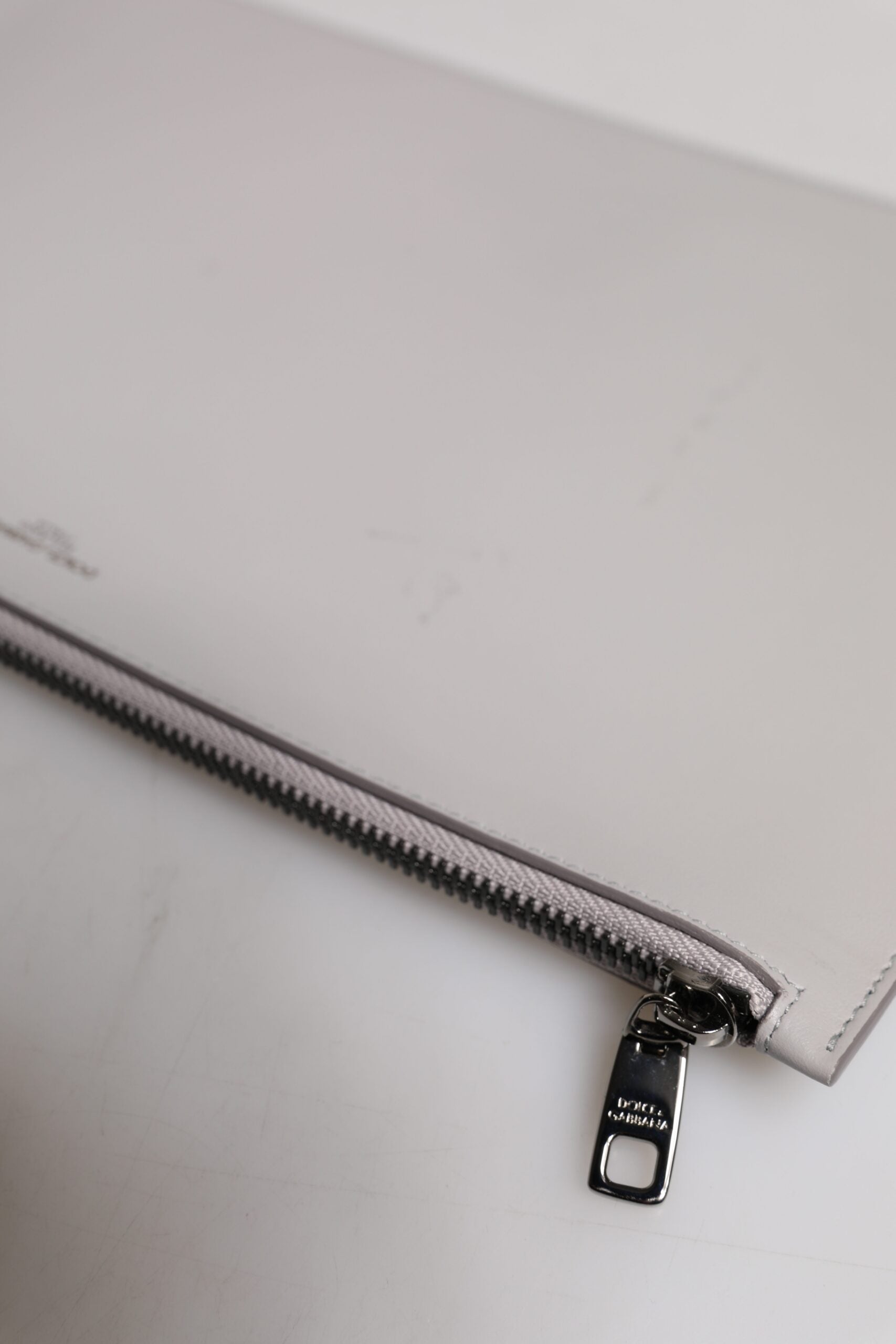 Pochette homme en cuir gris Dolce & Gabbana avec logo DG, fermeture éclair, design élégant et sophistiqué.