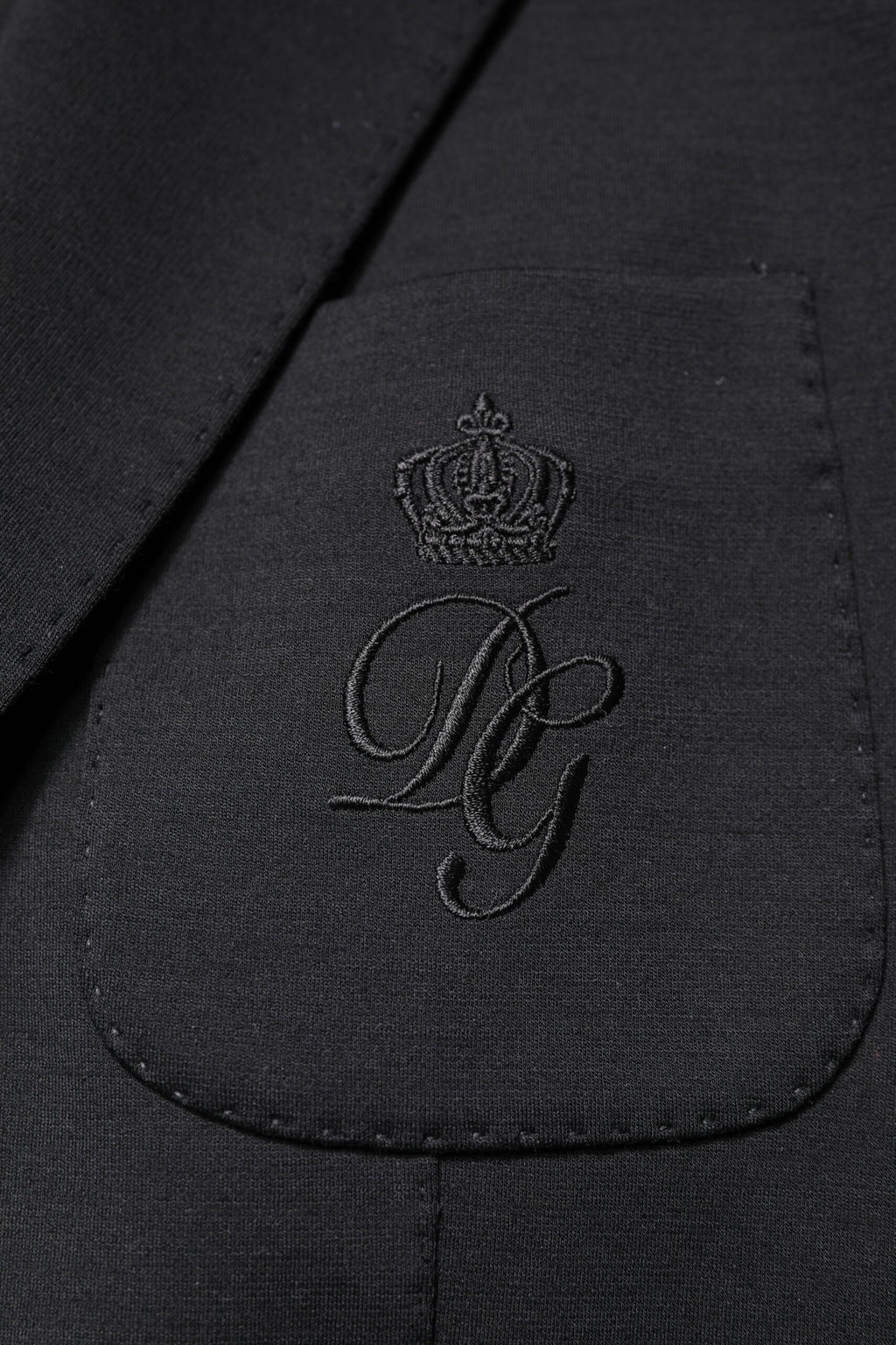 Manteau homme noir Dolce & Gabbana à un seul boutonnage, blazer élégant en tissu chic, porté sur un fond neutre.