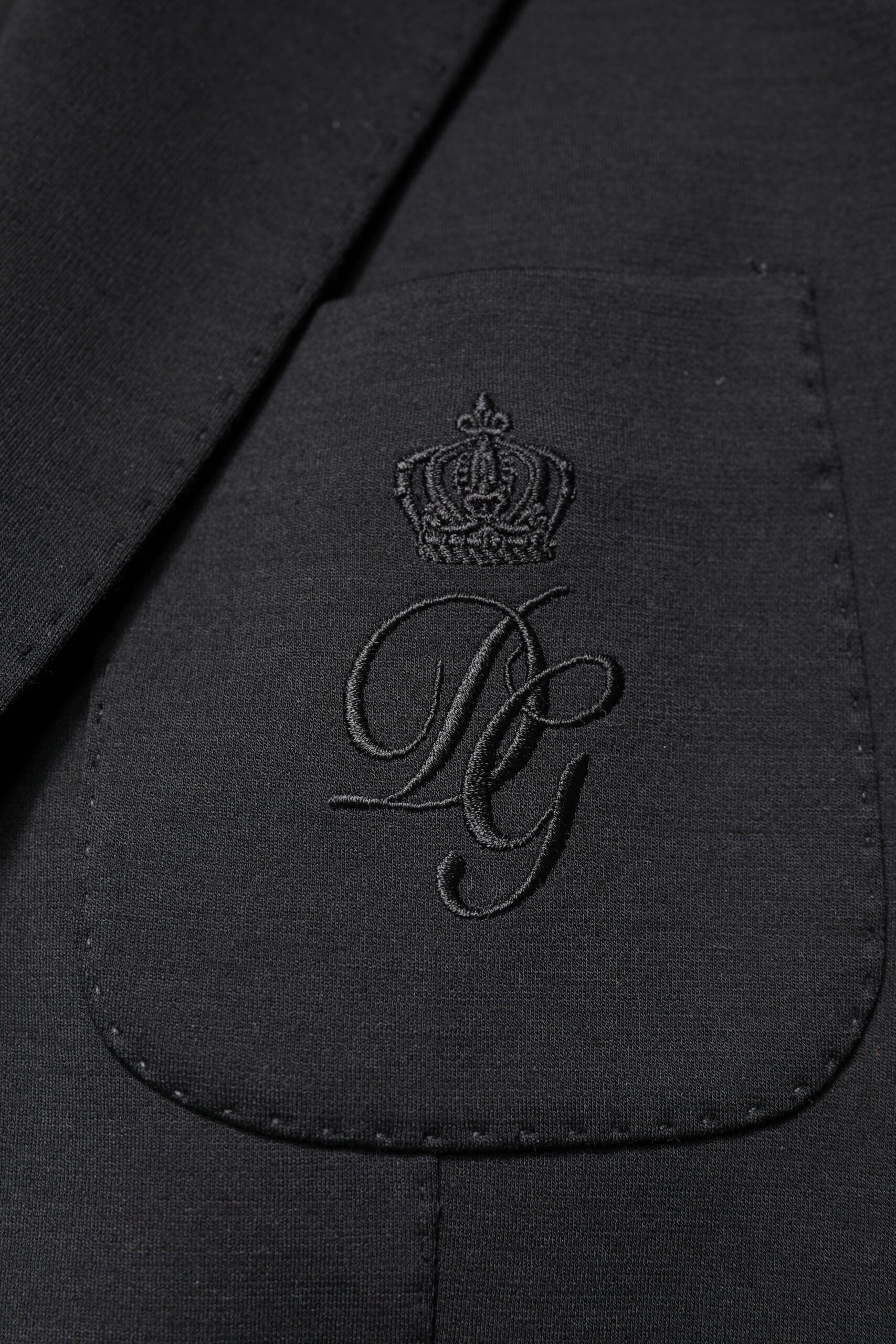 Manteau homme noir Dolce & Gabbana à un seul boutonnage, blazer élégant en tissu chic, porté sur un fond neutre.