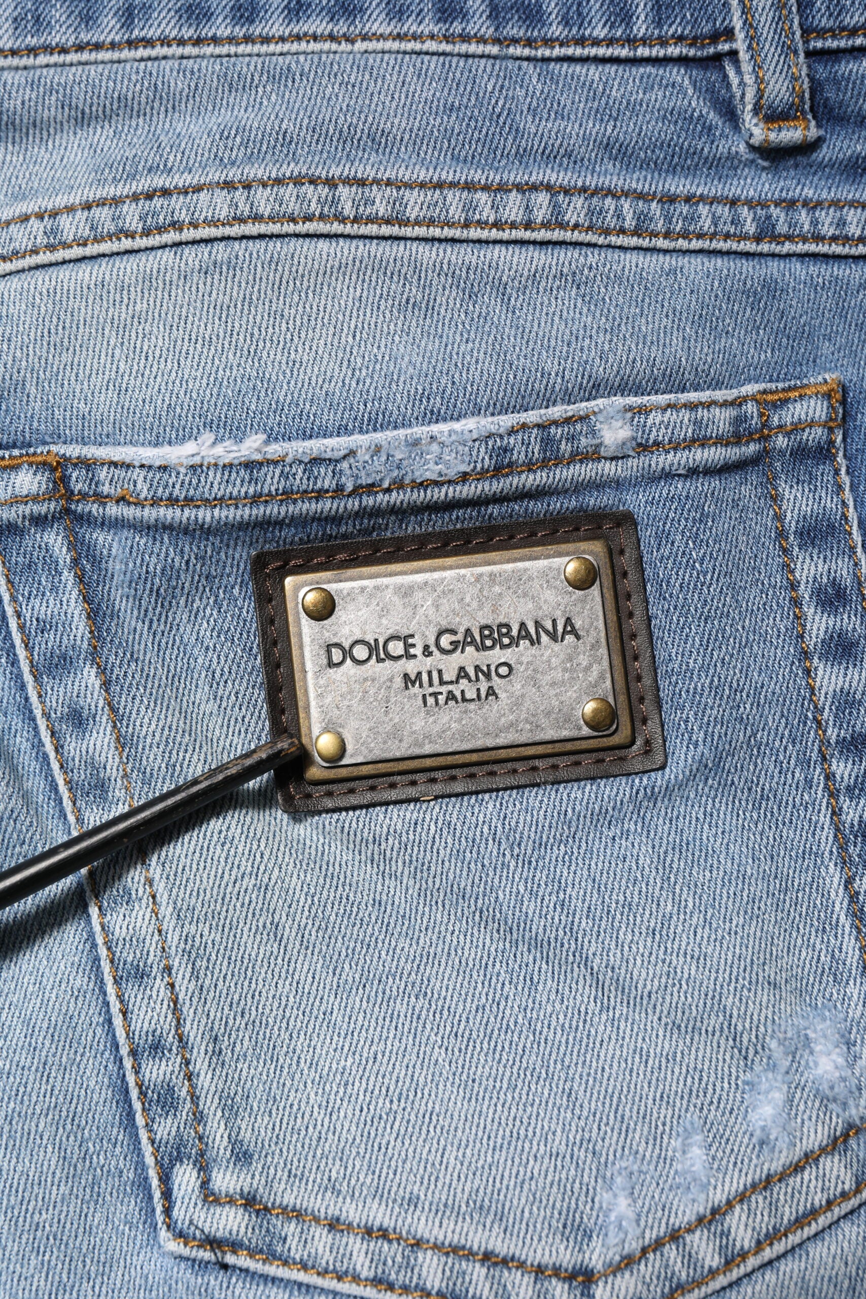 Jeans en denim bleu Dolce & Gabbana avec logo, ourlet déchiré et aspect vintage, style décontracté et tendance.