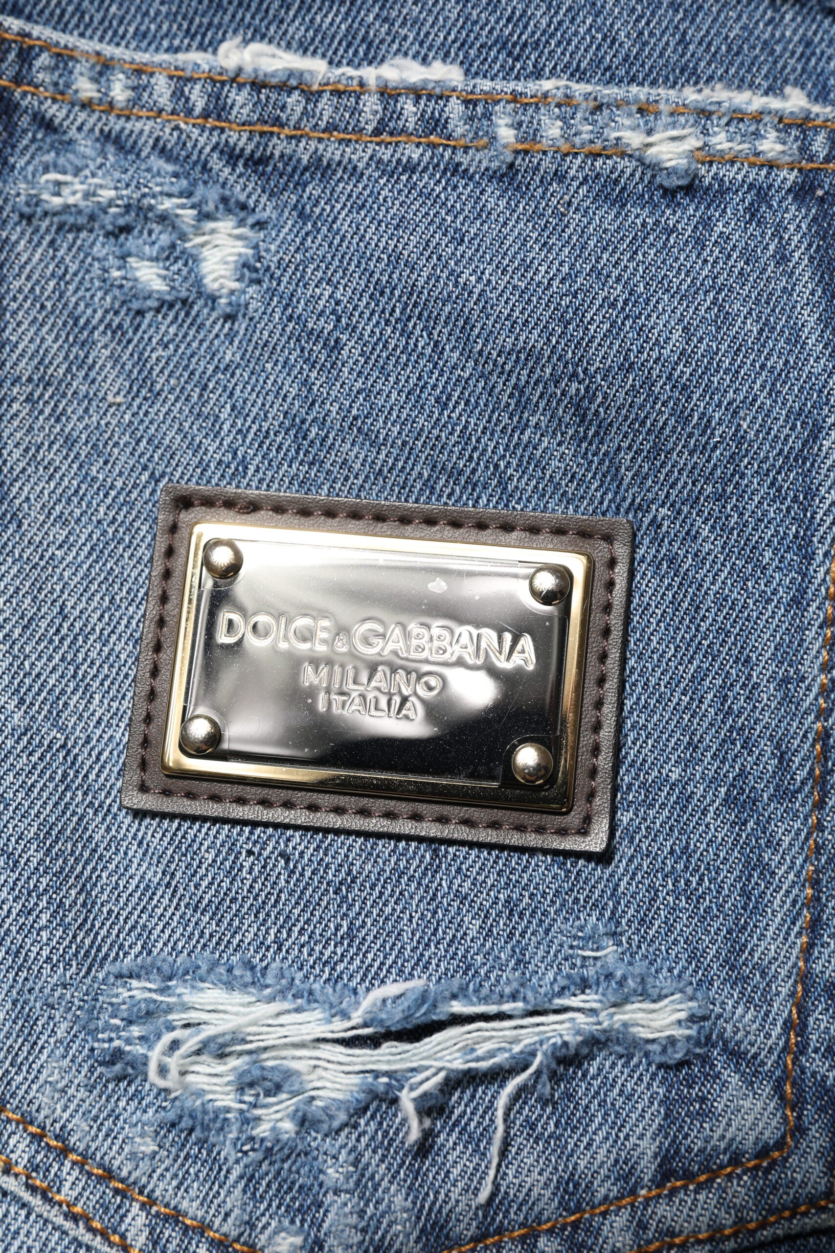 Jeans en denim bleus Dolce & Gabbana avec logo en plaque en coton déchiré et détails usés, style décontracté et tendance.