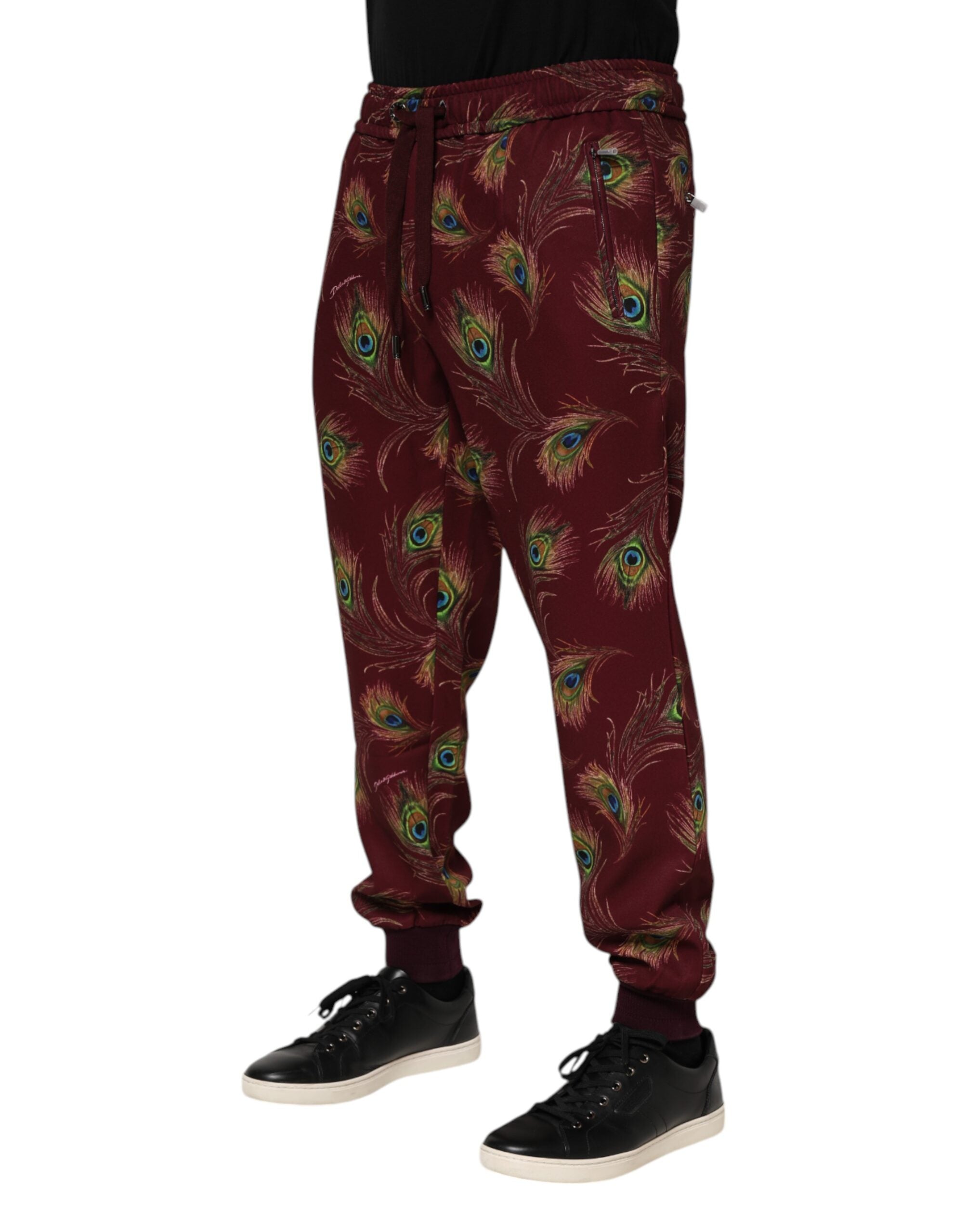 Pantalons joggers Dolce & Gabbana en velours bordeaux avec motif plumes de paon, coupe décontractée et détails élégants.