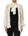 Haut Dolce & Gabbana blanc avec logo monogramme et col ascot, détails élégants et motif distinctif visible sur l'image.