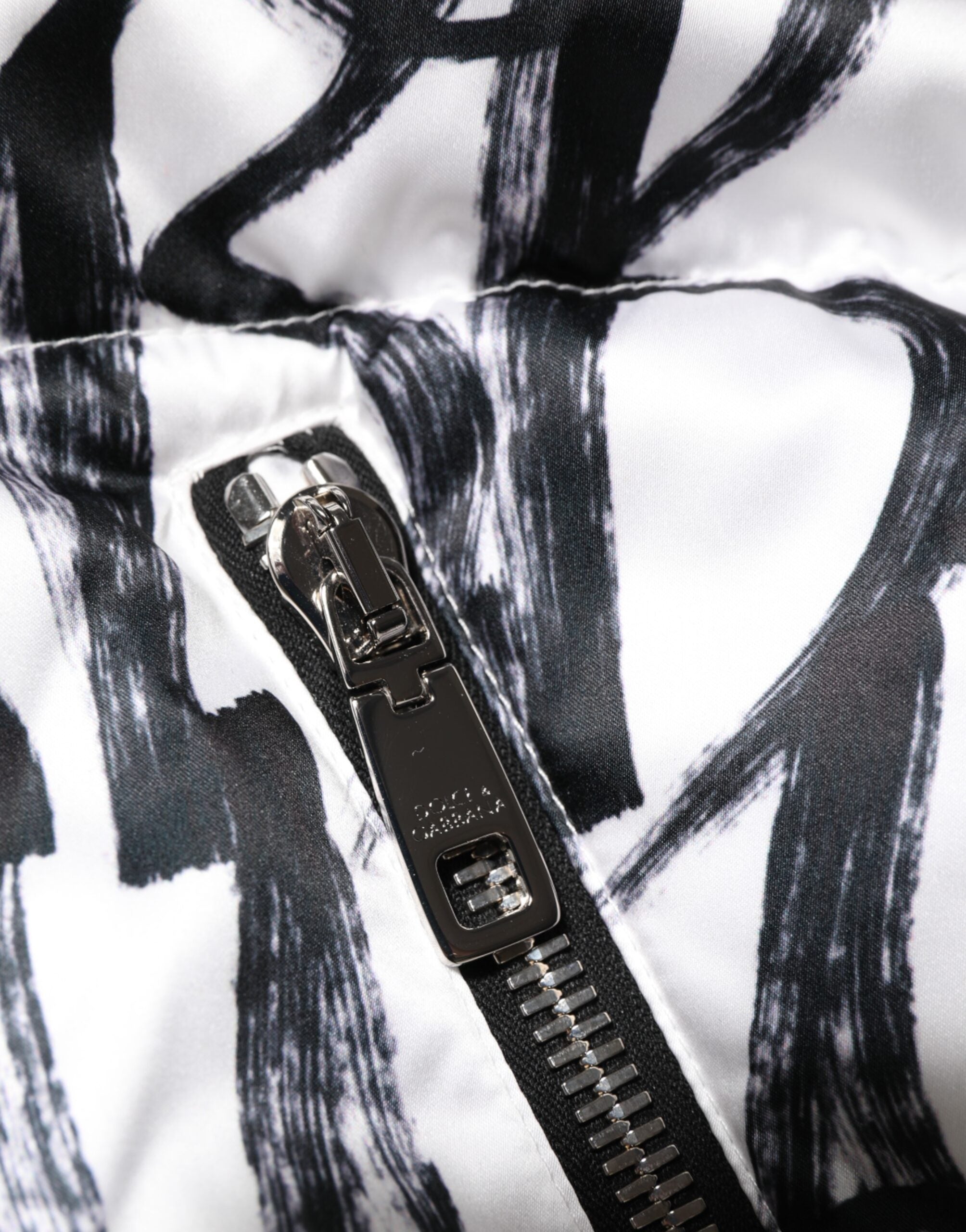 Veste puffer bomber Dolce & Gabbana blanche et noire avec logo graffiti, style tendance et design contemporain.