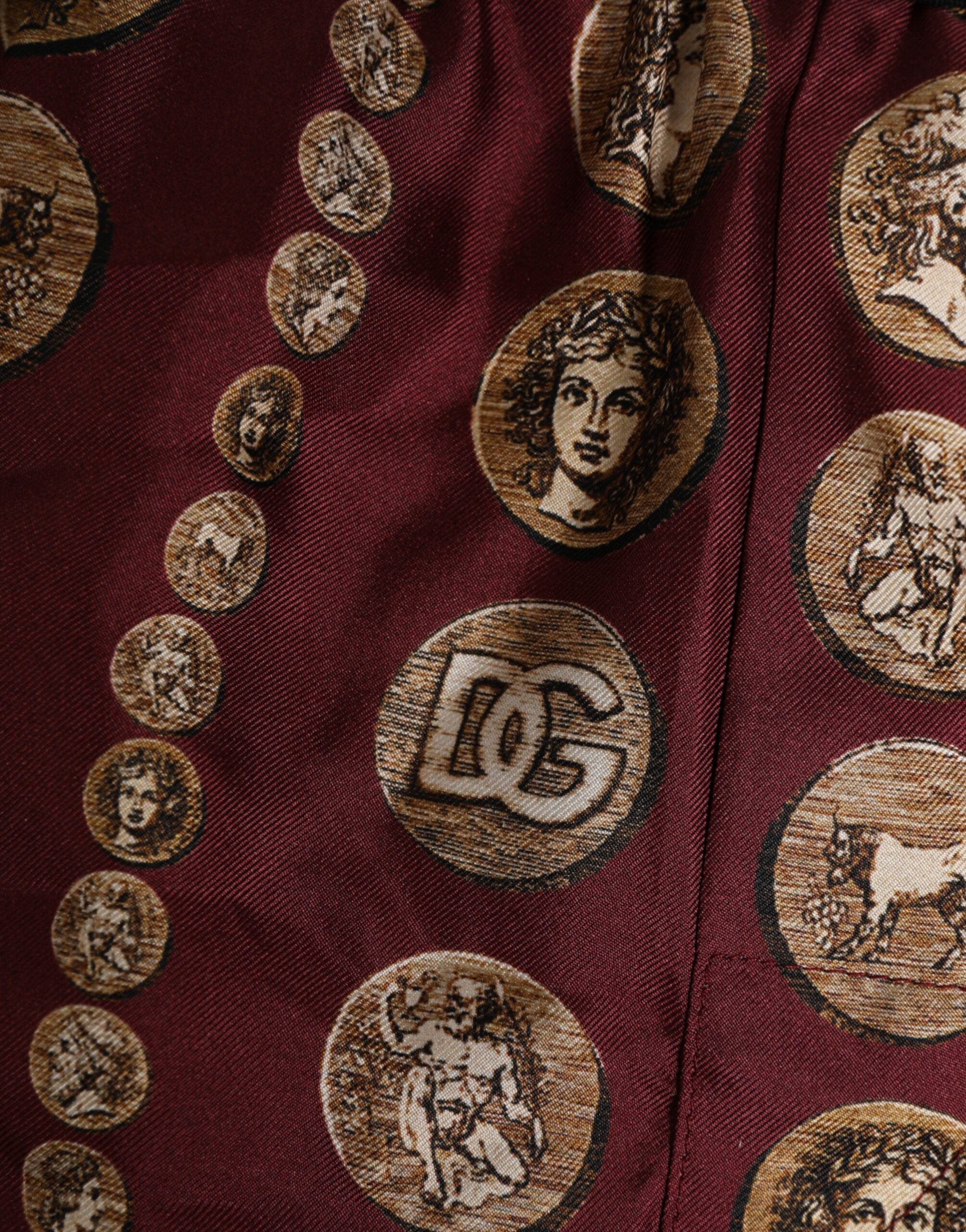 Boxers de bain homme Dolce & Gabbana en soie bordeaux avec motif pièces de monnaie, coupe courte et élégante.