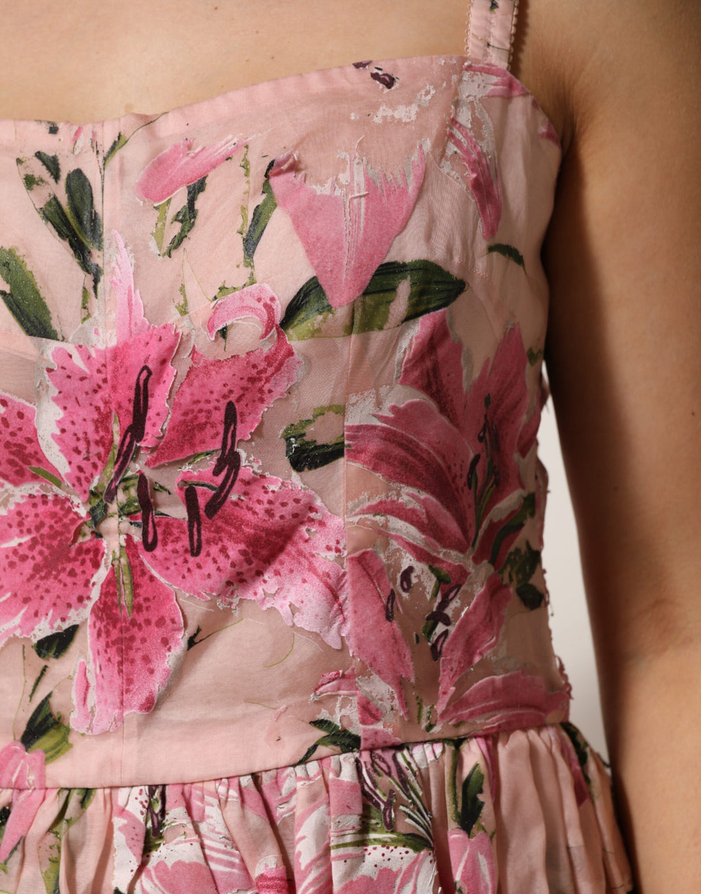 Robe sans manches en coton rose à fleurs et plis de Dolce & Gabbana, élégante et estivale, portée par une femme.