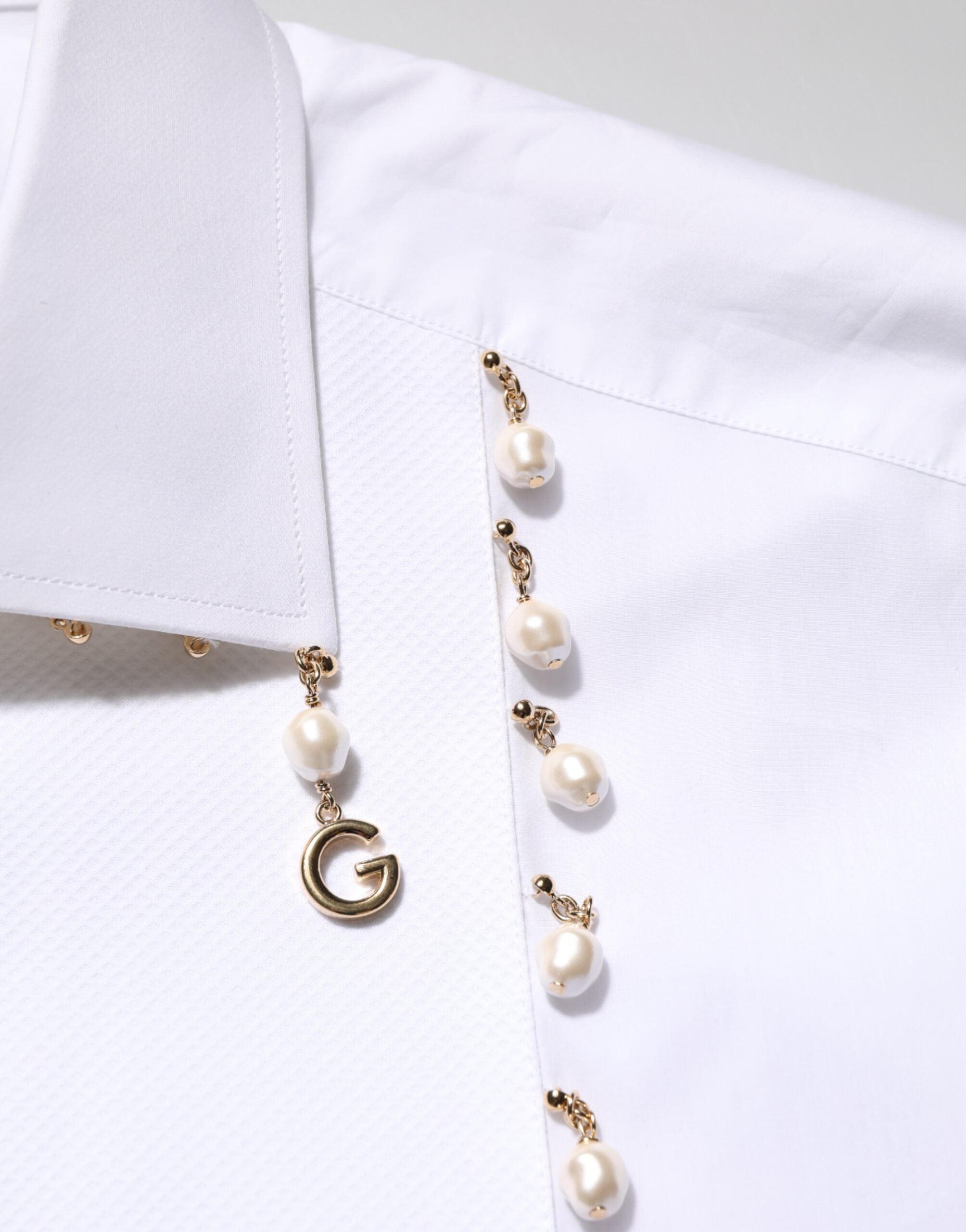Chemise formelle blanche Dolce & Gabbana en coton avec logo DG, perles et détails dorés visibles sur l'image.