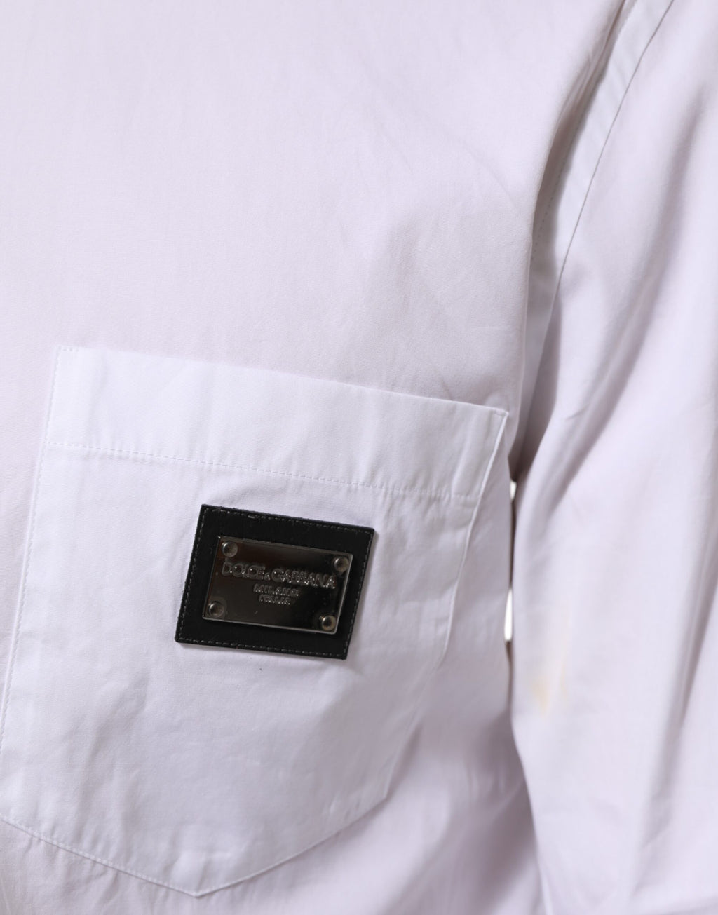 Chemise formelle blanche Dolce & Gabbana avec plaque logo, col élégant et coupe sophistiquée, visible en gros plan.