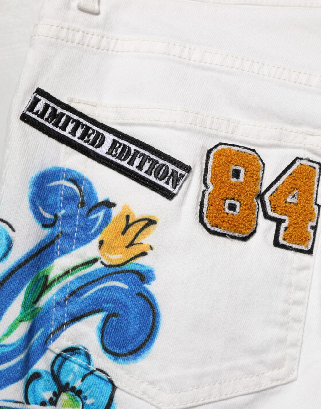 Jeans skinny en denim doré avec motif graffiti blanc de Dolce & Gabbana, style moderne et tendance.
