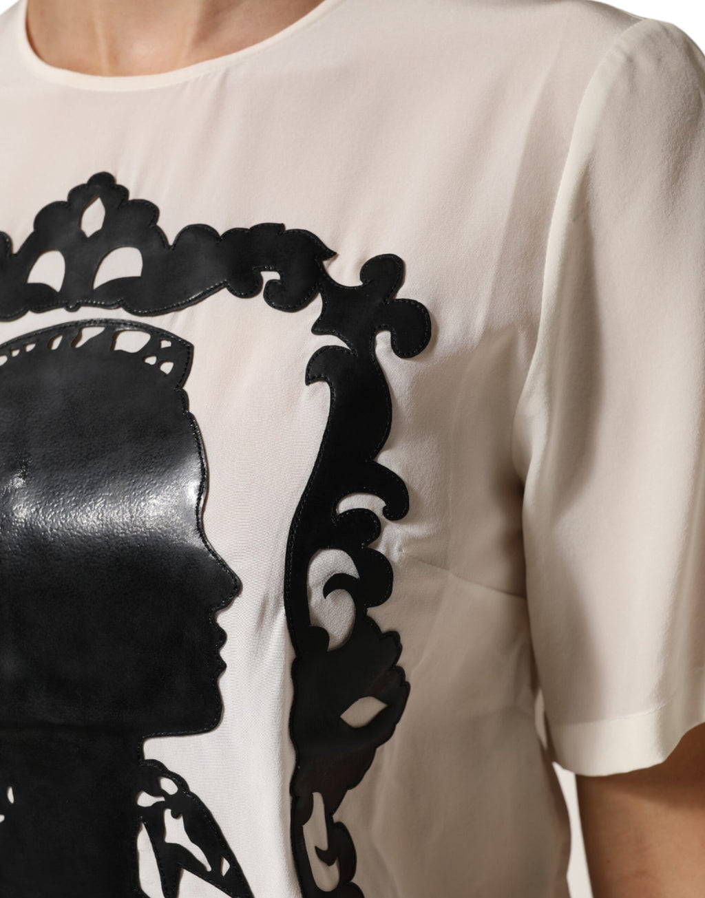 Haut Dolce & Gabbana en soie crème avec silhouette détaillée et manches courtes, visible en gros plan.
