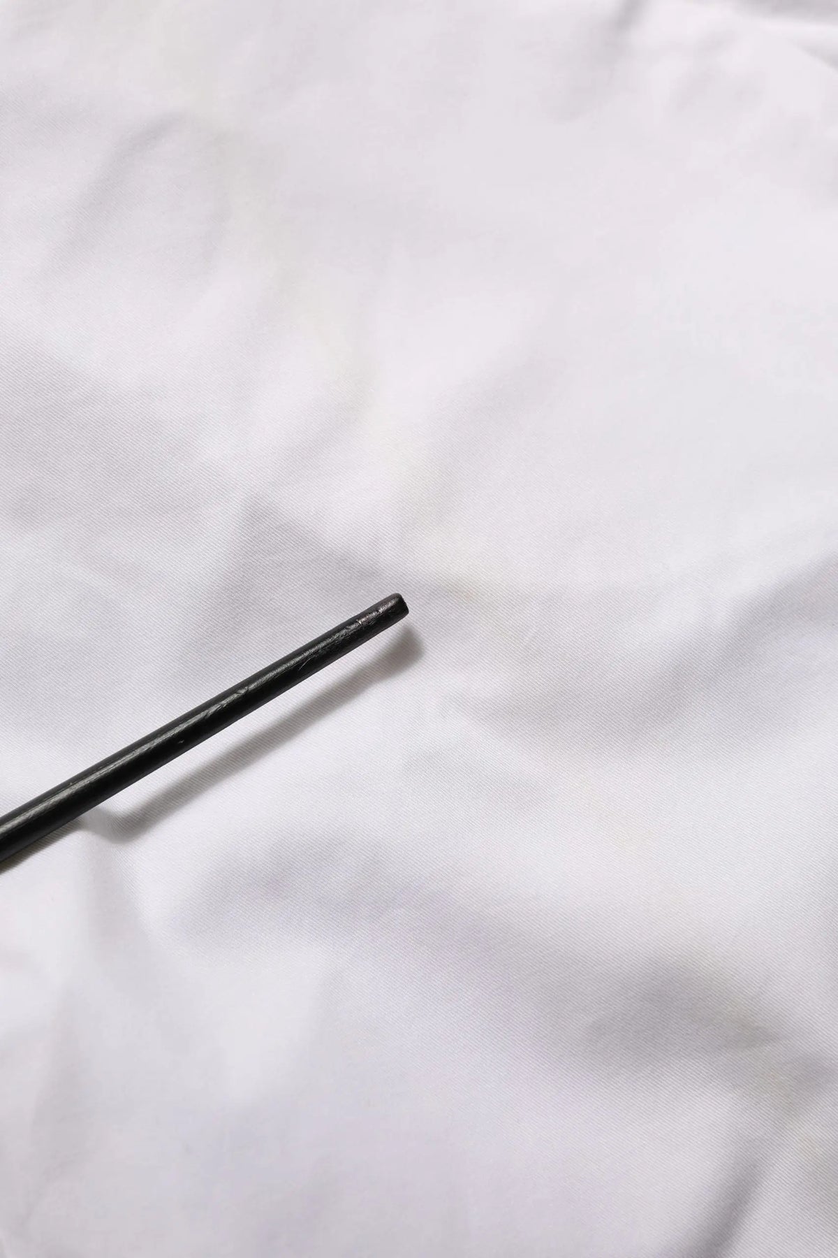 Bâtons noirs posés sur un tissu blanc à côté d’un pantalon blanc mi-tailleur en coton extensible armani jeans