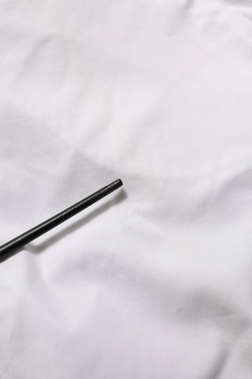 Bâtons noirs posés sur un tissu blanc à côté d’un pantalon blanc mi-tailleur en coton extensible armani jeans