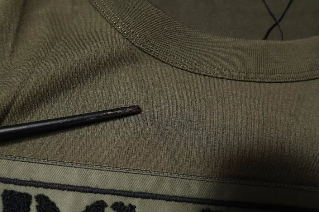 Une baguette en bois foncé posée sur un t shirt dolce & gabbana vert armée en coton col rond