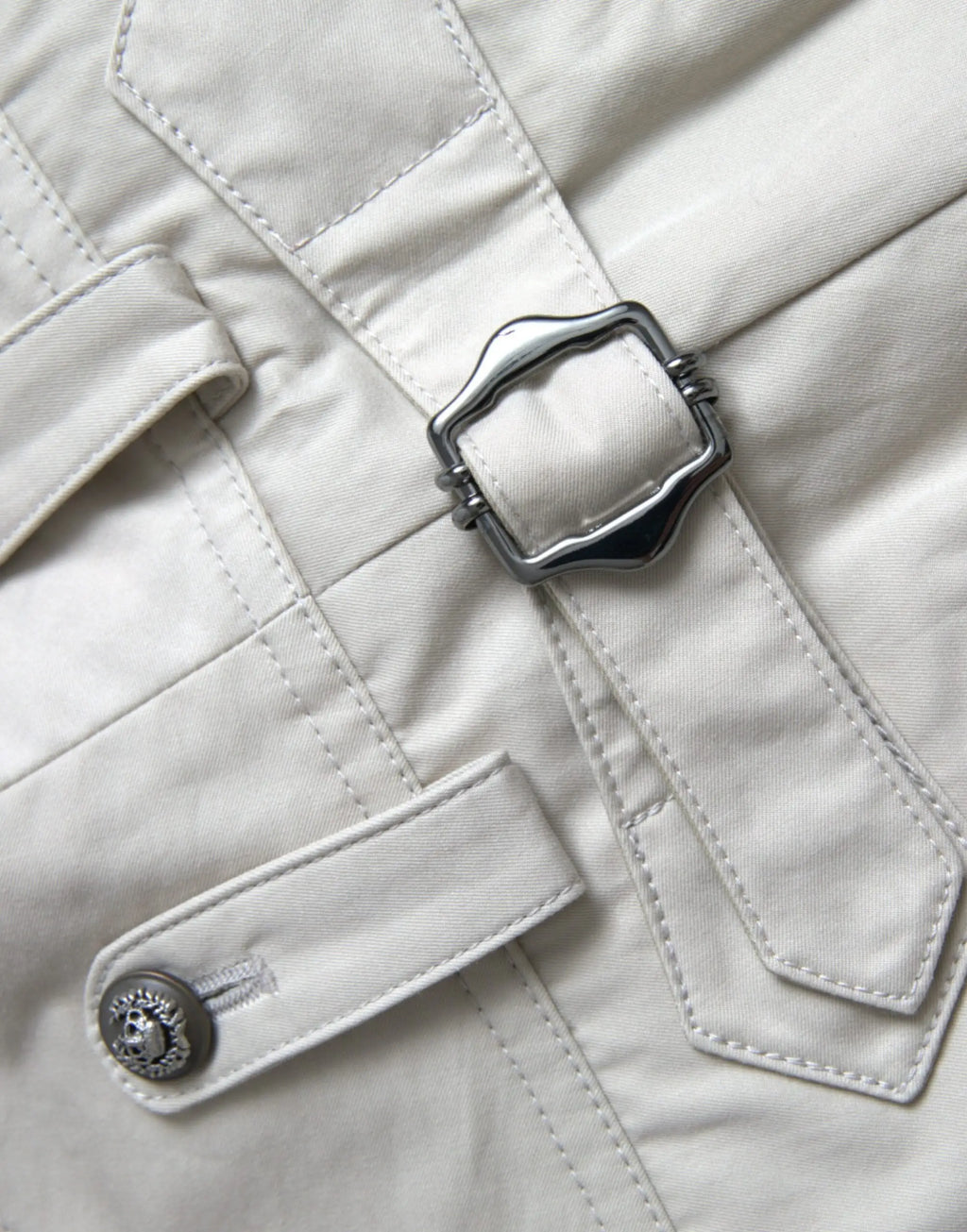 Manteau trench couleur crème avec boucle argentée en forme de bouclier et bouton orné assorti porté avec pantalon beige dolce & gabbana en coton taille haute fuselée