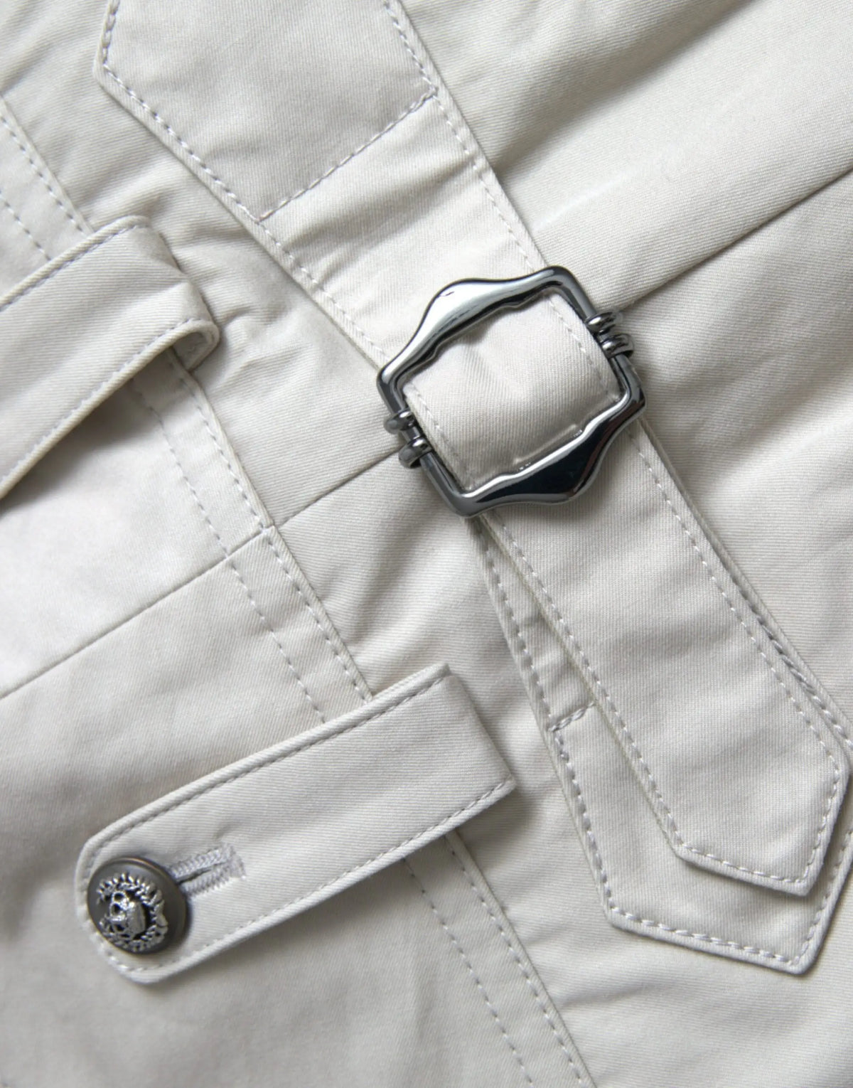 Manteau trench couleur crème avec boucle argentée en forme de bouclier et bouton orné assorti porté avec pantalon beige dolce & gabbana en coton taille haute fuselée