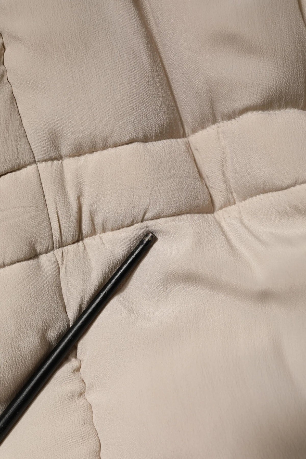 Un objet cylindrique noir repose en diagonale sur un tissu matelassé beige du trench long beige dolce & gabbana