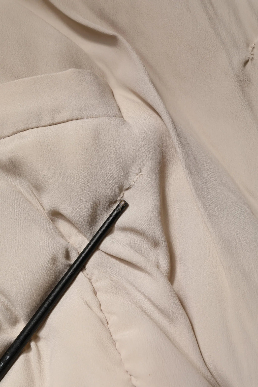 Crayon noir reposant sur tissu crème déchiré d’un manteau trench long beige matelassé à col dolce & gabbana