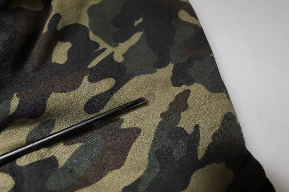 Un objet cylindrique noir posé sur un tissu camouflage vert marron et gris foncé pour sweat à capuche dolce & gabbana